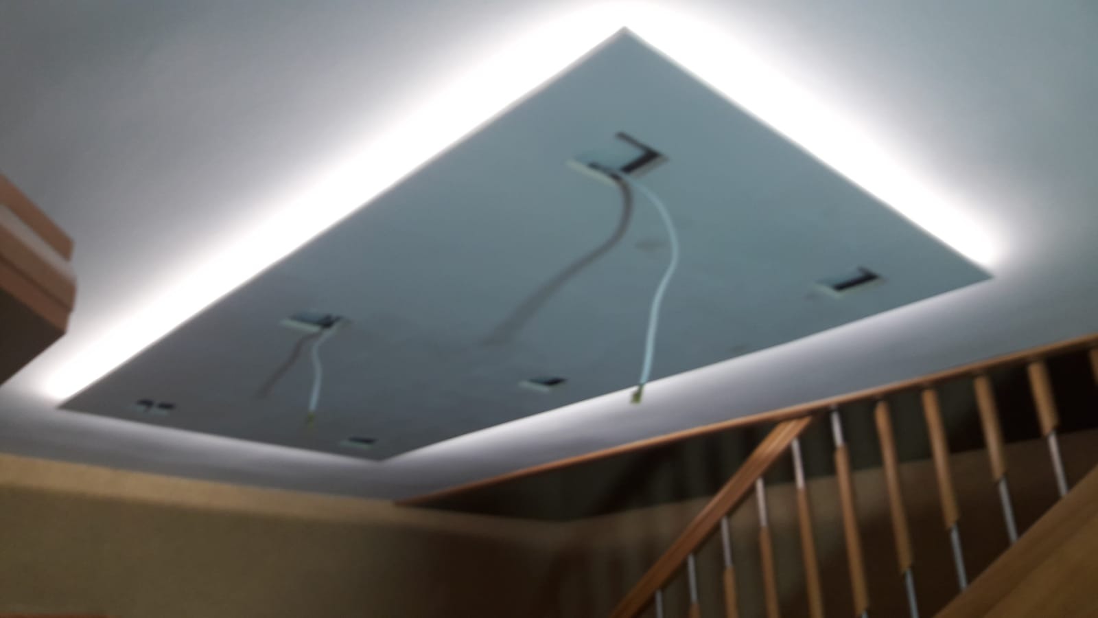 Podwieszany sufit z płyty z oświetleniem LED, widoczne kable, fragment schodów w tle. Kształt sufitu prostokątny z zaokrąglonymi rogami.