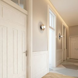 Firma JFK - Białe, klasyczne drzwi z ozdobnymi panelami ściennymi w jasnym korytarzu. Geometryczna podłoga i nowoczesne oświetlenie dodają elegancji.