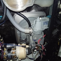 FIXIT SERWIS - Wnętrze zmywarki w trakcie naprawy: widoczne elementy pompy, węże, okablowanie i zbiornik na wodę. Detal techniczny z bliska, ukazujący skomplikowaną budowę urządzenia.