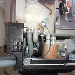 FIXIT SERWIS - Wnętrze zmywarki w trakcie naprawy: widoczne węże, zbiorniki, elementy elektroniczne i narzędzie Yato. Detal mechanizmu z bliska, ukazujący skomplikowaną budowę urządzenia.