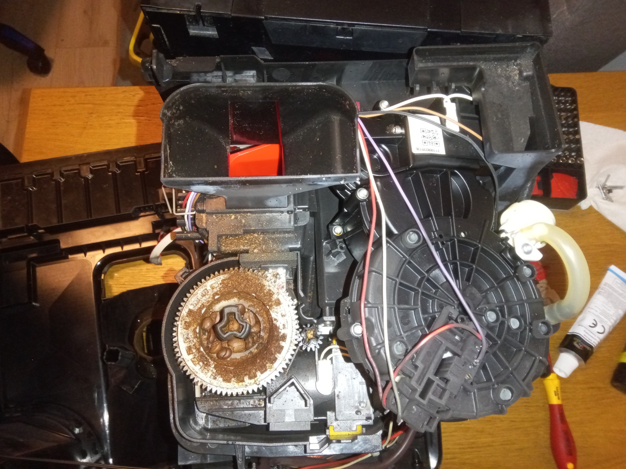 Wnętrze rozmontowanego ekspresu do kawy z widocznymi elementami mechanicznymi, przewodami i narzędziami, sugerujące etap naprawy lub konserwacji urządzenia.