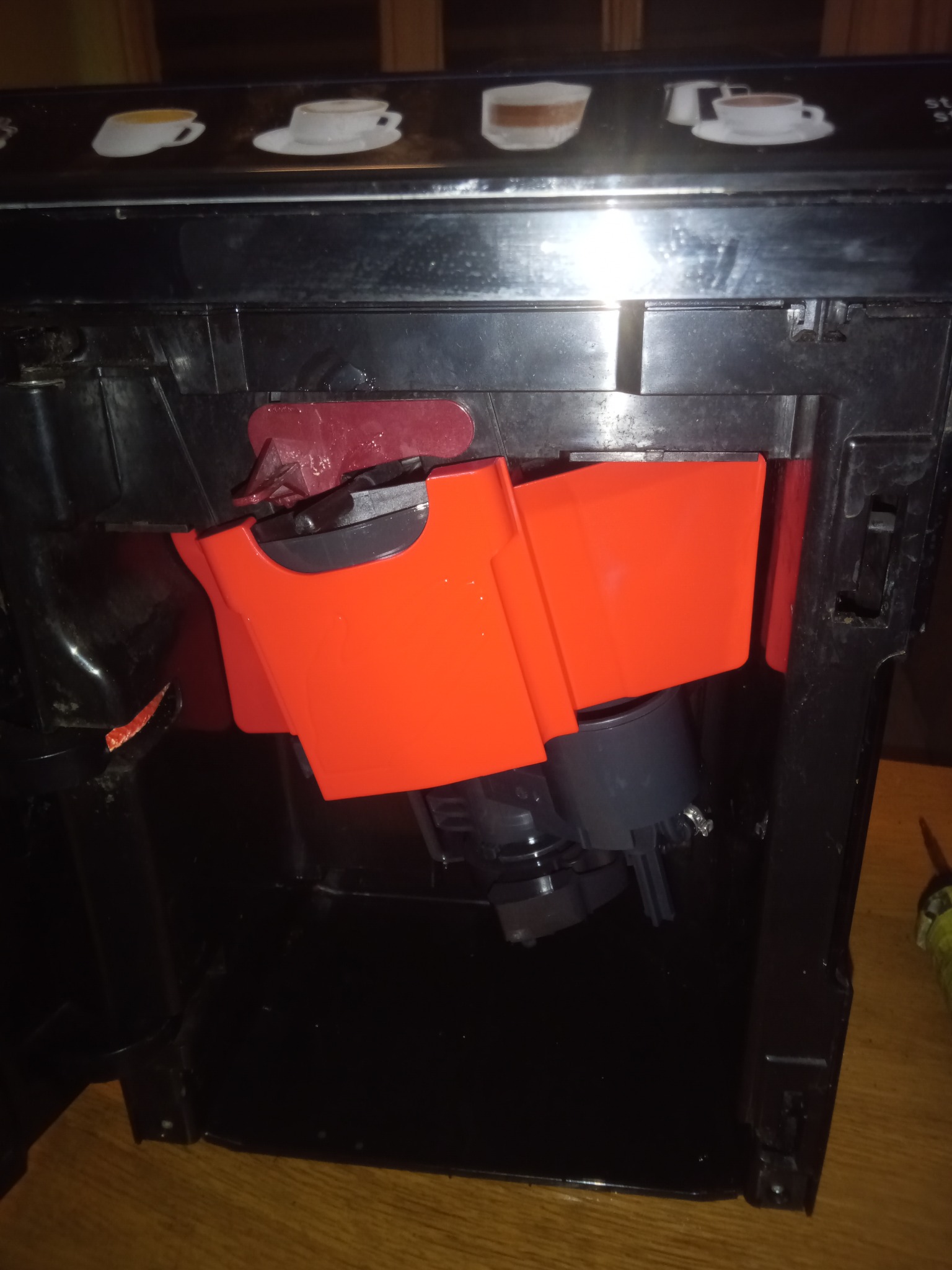 Wnętrze ekspresu do kawy z widocznymi elementami konstrukcyjnymi i pomarańczowymi pojemnikami. Widoczne ślady użytkowania i demontażu.