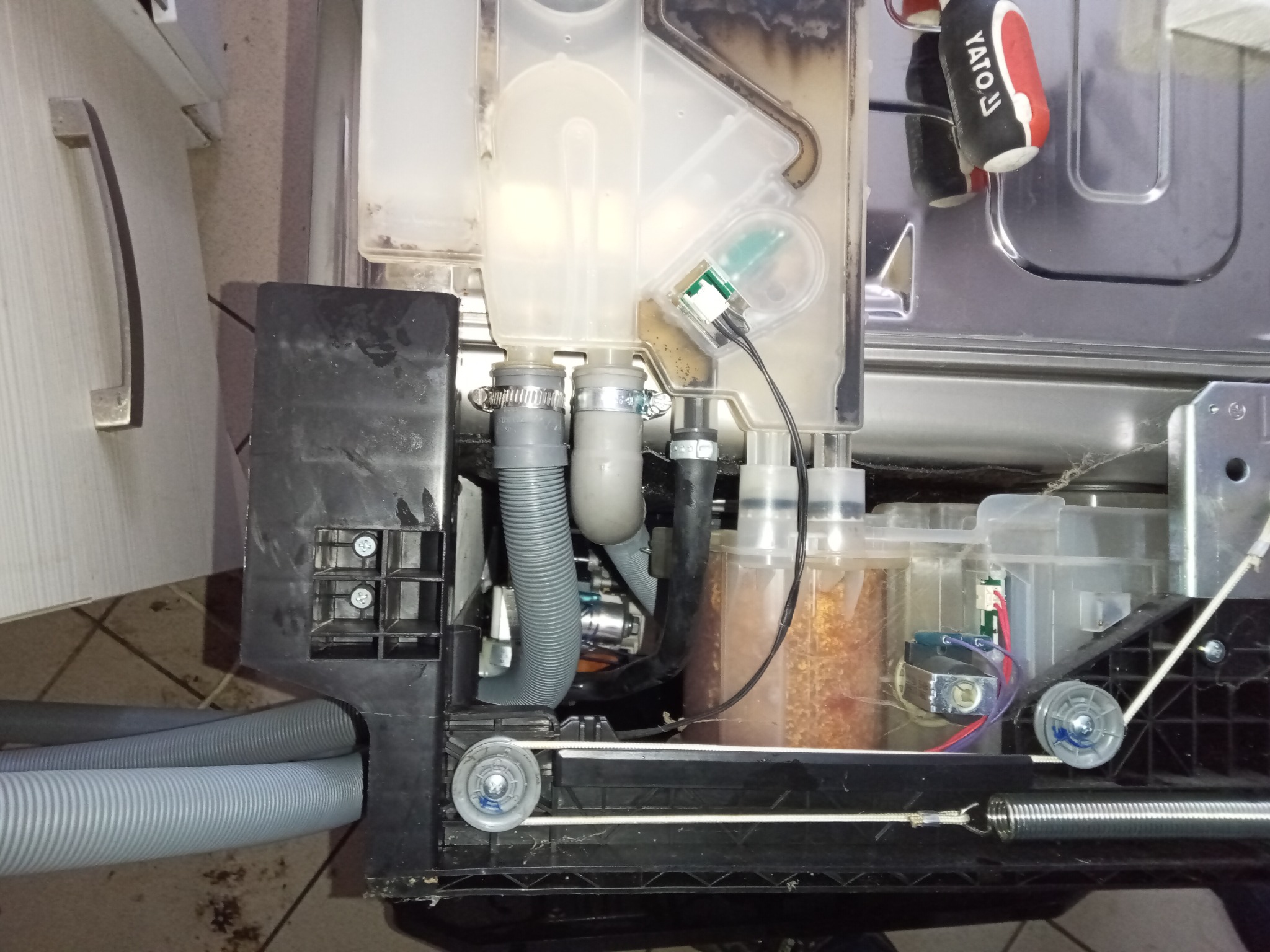 Wnętrze zmywarki w trakcie naprawy: widoczne węże, zbiorniki, elementy elektroniczne i narzędzie Yato. Detal mechanizmu z bliska, ukazujący skomplikowaną budowę urządzenia.