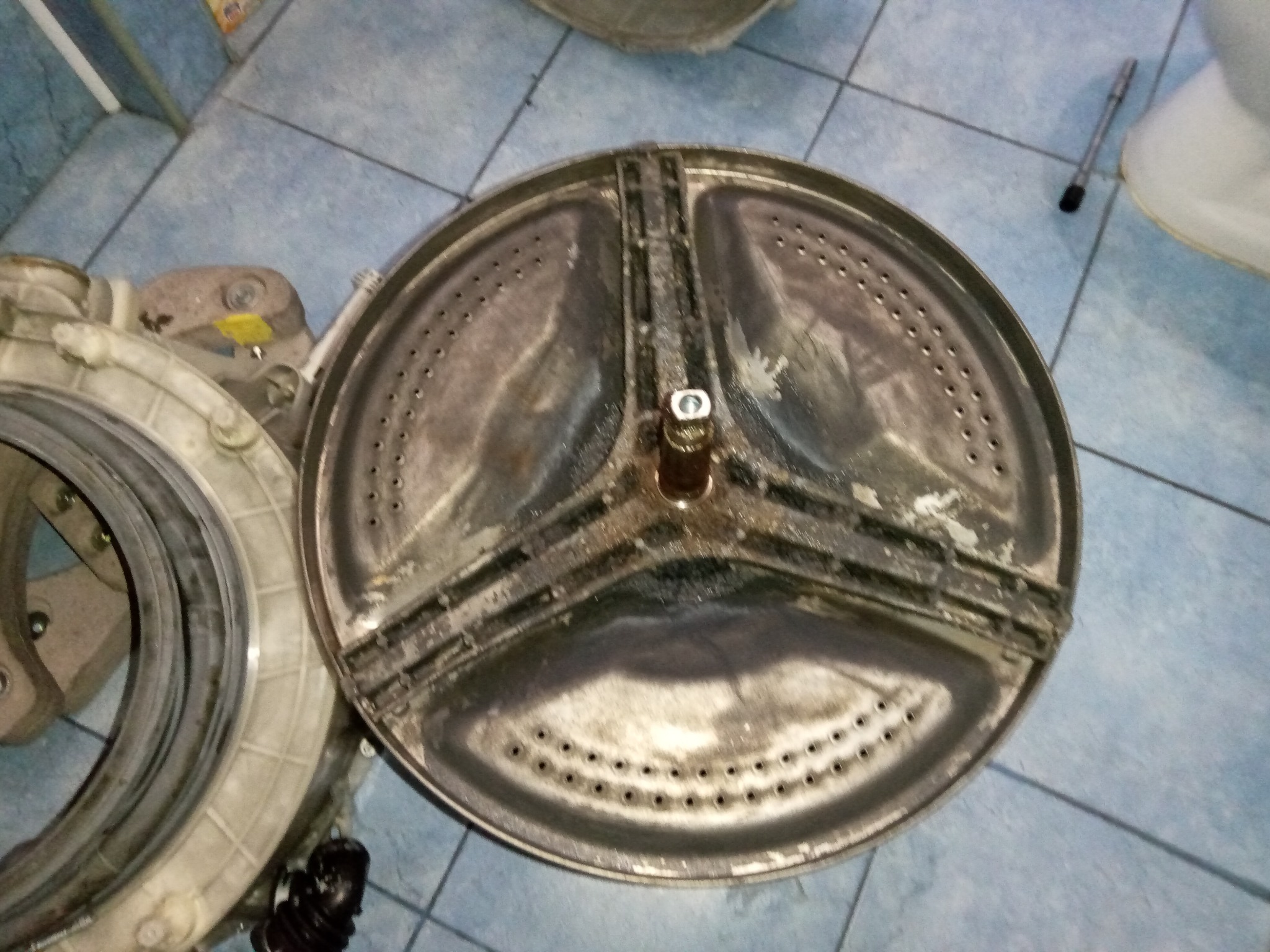 Bęben pralki po demontażu, widoczne ślady użytkowania. Usługa naprawy pralek w Jaśle. Elementy pralki na tle niebieskich płytek.