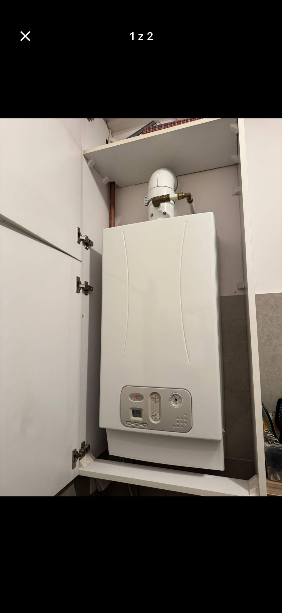 Biały piec gazowy w szafce, widoczne przyłącza i panel sterowania. Ujęcie z bliska, oświetlenie dzienne, wnętrze pomieszczenia.