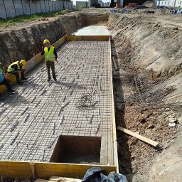 Wladyslaw Chepeluiev - Zbrojenie fundamentu pod budynek przemysłowy, widoczne szalunki i stalowe pręty tworzące siatkę. Pracownicy w kaskach i kamizelkach odblaskowych nadzorują prace.