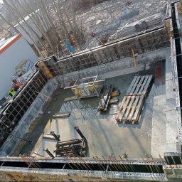 Wladyslaw Chepeluiev - Zalane fundamenty z deskowaniem i zbrojeniem, widok z góry. Na budowie obecni pracownicy w odblaskowych kamizelkach i kaskach. Widoczne palety i narzędzia.