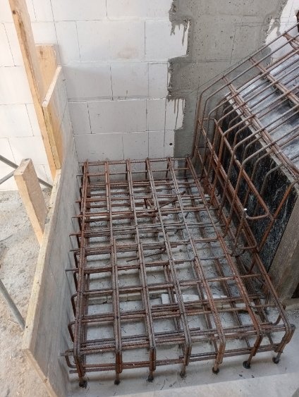 Siatka zbrojeniowa w szalunku, przygotowana do zalania betonem. Widoczne bloczki betonowe w tle. Kąt ujęcia z góry, podkreślający regularność siatki.