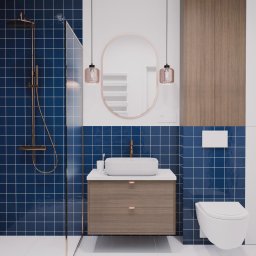 Kwartał Studio Projektowe Mateusz Bidas - Nowoczesna łazienka z niebieskimi płytkami, kabiną prysznicową ze złotą armaturą, owalnym lustrem i drewnianą szafką pod umywalką. Widoczna pralka i toaleta.