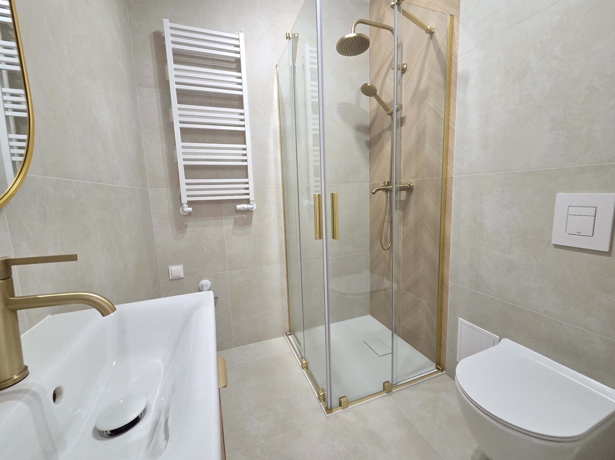 Wykończona łazienka w Buszkowicach: kabina prysznicowa ze złotymi detalami, umywalka i toaleta w jasnej tonacji. Nowoczesny design i funkcjonalność.