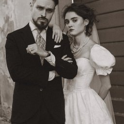 MORGAN & NESS - Sepiowy portret pary: mężczyzna w ciemnym garniturze z wzorzystym krawatem, kobieta w białej sukni ślubnej z perłami, oboje z poważnym wyrazem twarzy na tle ściany.