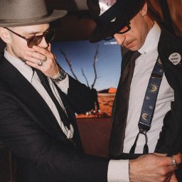 MORGAN & NESS - Dwóch mężczyzn w eleganckich strojach: jeden w szarym kapeluszu i garniturze, drugi w czarnym kapeluszu, koszuli i szelkach z motywem księżyca. Nietypowe stylizacje.