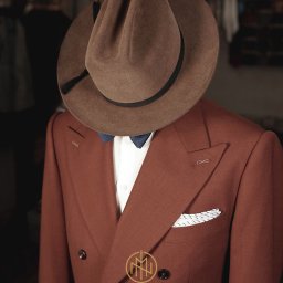 MORGAN & NESS - Brązowy, dwurzędowy garnitur z muchą i poszetką, nakryty brązowym kapeluszem. Elegancki strój na manekinie w krawieckim atelier.