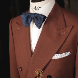 MORGAN & NESS - Brązowy, dwurzędowy garnitur z granatową muchą i poszetką, prezentowany na manekinie krawieckim z logo 'Tailor N.Y.', w eleganckim, stonowanym oświetleniu.