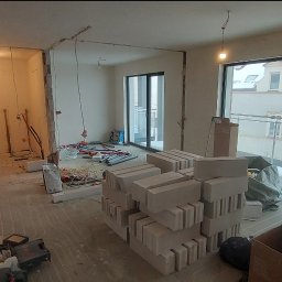 Kamil Dziupiński - Wnętrze w trakcie remontu: widoczne materiały budowlane, instalacje i narzędzia. Prace przygotowawcze przed wykończeniem, z widokiem na zaśnieżony krajobraz za oknem.