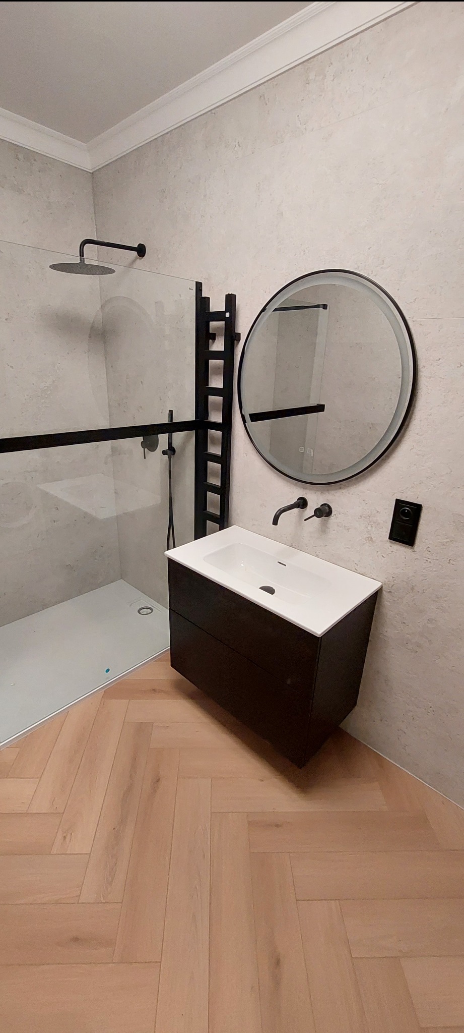 Nowoczesna łazienka z kabiną typu walk-in, umywalką nablatową na szafce w kolorze ciemnego drewna, okrągłym lustrem z podświetleniem LED i grzejnikiem drabinkowym.