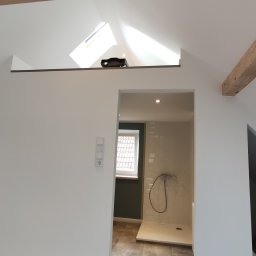 Azariasz Janicki ZIAJ-TECH - Jasne poddasze z drewnianymi belkami i widokiem na łazienkę z kabiną prysznicową. Świeżo pomalowane ściany i okno dachowe w tle.