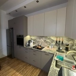 Katarzyna Mamorska - Szare meble kuchenne z blatem imitującym marmur, oświetlone punktowo, z widocznym sprzętem AGD i akcesoriami kuchennymi. Ujęcie z perspektywy narożnej.