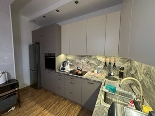 Szare meble kuchenne z blatem imitującym marmur, oświetlone punktowo, z widocznym sprzętem AGD i akcesoriami kuchennymi. Ujęcie z perspektywy narożnej.