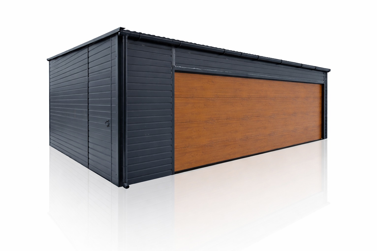 Garaż blaszany z dachem dwuspadowym, w kolorze grafitowym z drewnopodobną bramą segmentową, na białym tle z odbiciem. Widoczny zamek w drzwiach bocznych.