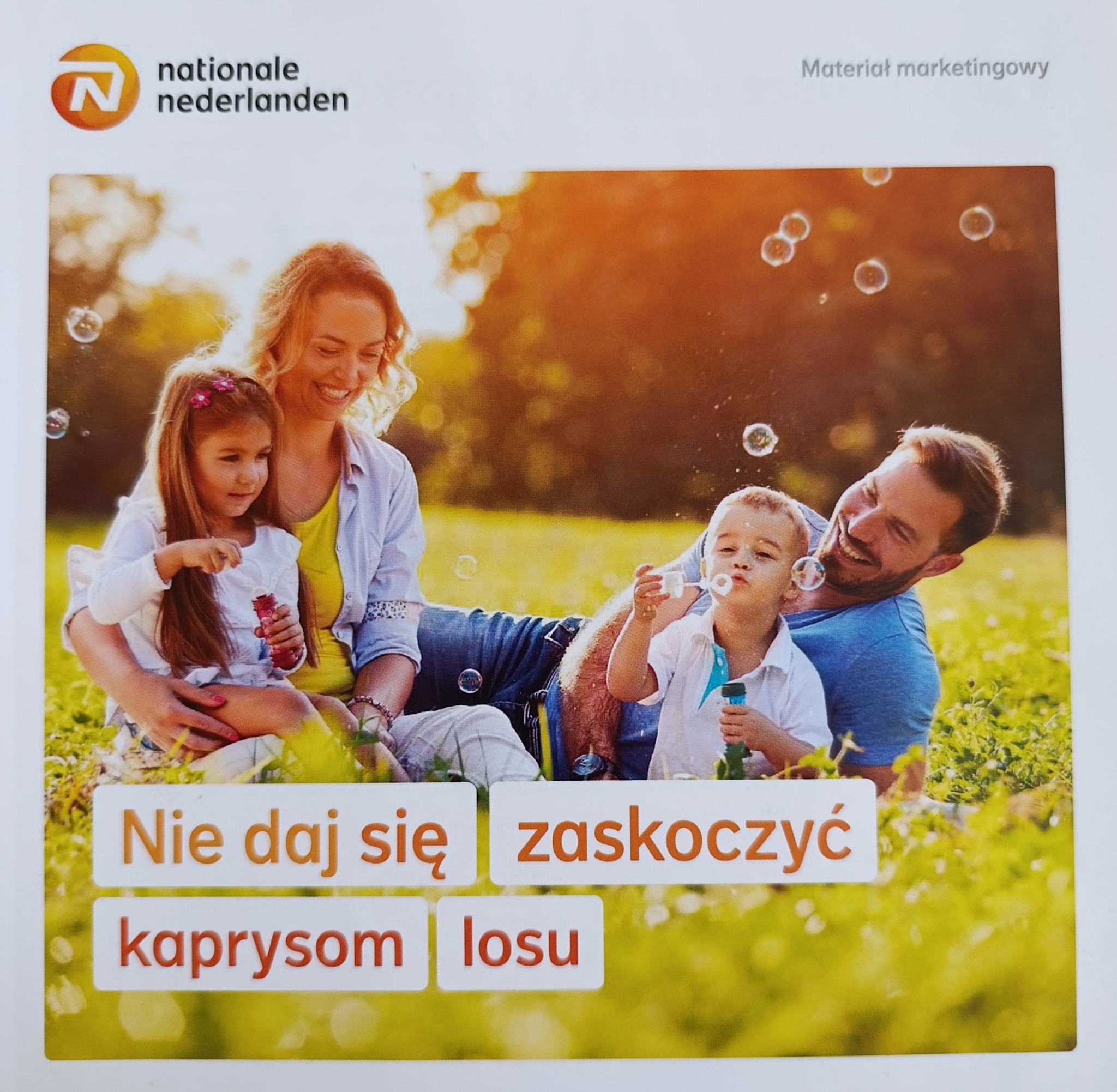 Uśmiechnięta rodzina puszcza bańki na tle zieleni. Materiał marketingowy Nationale Nederlanden z hasłem 'Nie daj się zaskoczyć kaprysom losu'.