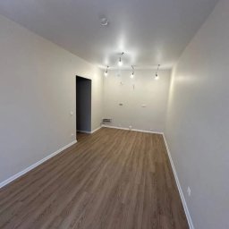 IOMA GROUP SPÓŁKA Z OGRANICZONĄ ODPOWIEDZIALNOŚCIĄ - Wykończone wnętrze po remoncie w Brzegu: parkiet w odcieniach brązu, świeżo pomalowane ściany w jasnym odcieniu i minimalistyczne oświetlenie sufitowe.