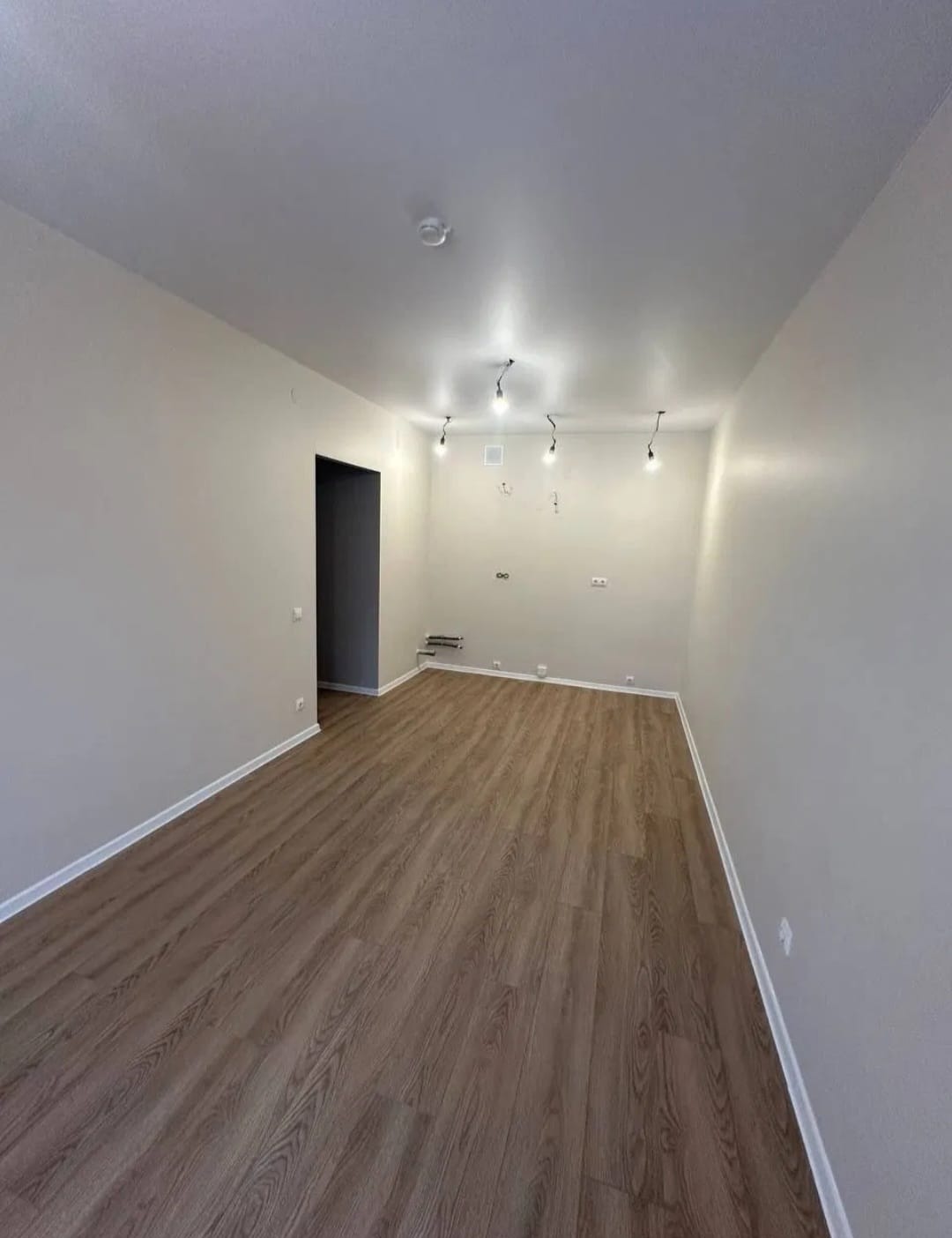 Wykończone wnętrze po remoncie w Brzegu: parkiet w odcieniach brązu, świeżo pomalowane ściany w jasnym odcieniu i minimalistyczne oświetlenie sufitowe.