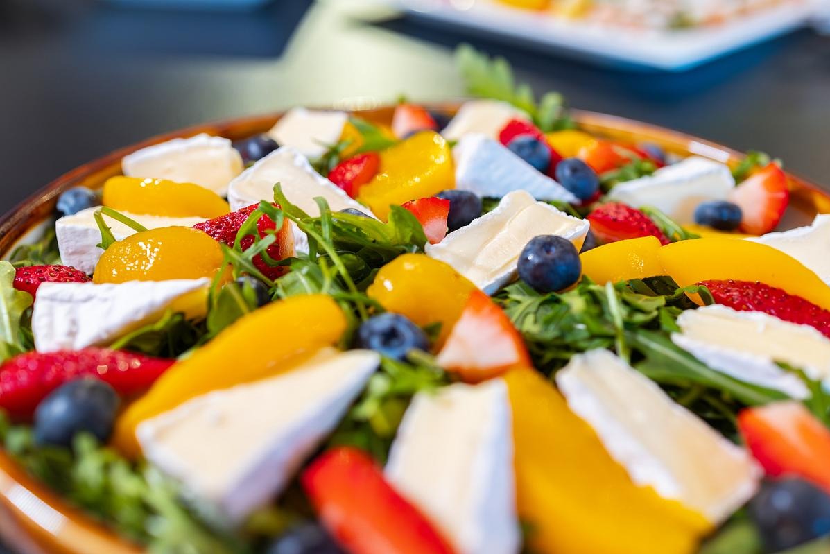 Kolorowa sałatka z rukolą, truskawkami, mango, borówkami i serem camembert na drewnianym talerzu, prezentowana z bliska w jasnym oświetleniu.