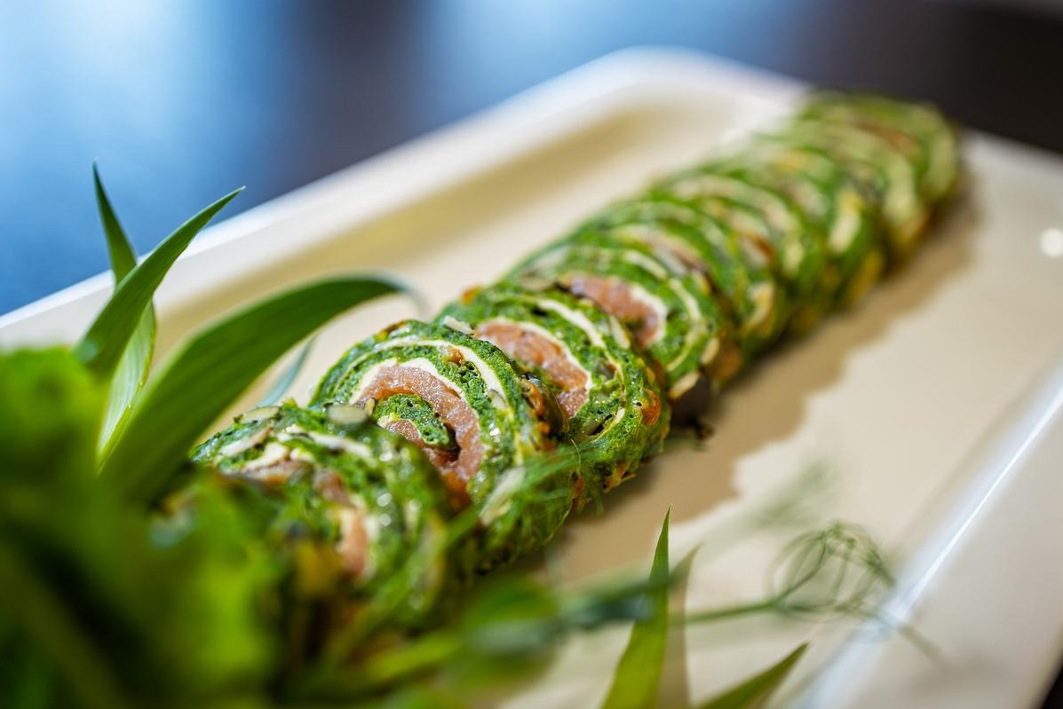 Apetyczne roladki ze szpinaku i łososia na białym talerzu, udekorowane świeżymi ziołami. Elegancka kompozycja kulinarna, idealna na catering.