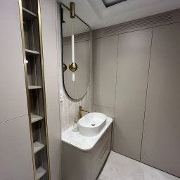 Mateusz Marcinkiewicz - Nowoczesna łazienka w beżach: owalna umywalka nablatowa, złota armatura, lustro z podświetleniem i szafki w zabudowie. Minimalistyczny design z marmurową podłogą.
