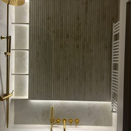 Mateusz Marcinkiewicz - Nowoczesna łazienka w Warszawie: złota armatura, podświetlane półki i dekoracyjne płytki ścienne tworzą elegancki klimat. Biały grzejnik drabinkowy.