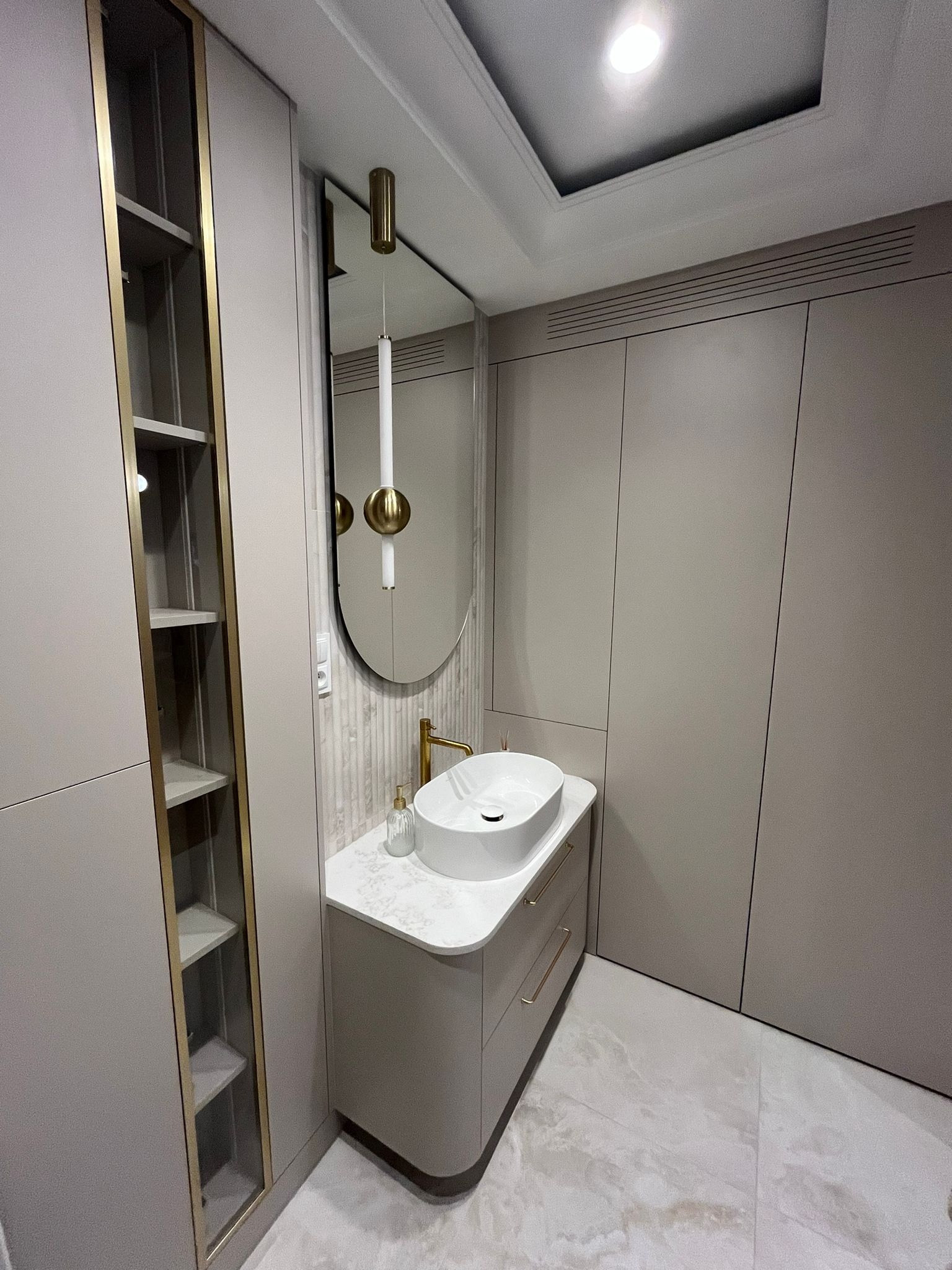 Nowoczesna łazienka w beżach: owalna umywalka nablatowa, złota armatura, lustro z podświetleniem i szafki w zabudowie. Minimalistyczny design z marmurową podłogą.