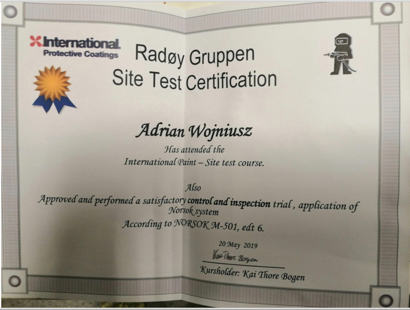 Certyfikat ukończenia kursu International Paint - Site Test dla Adriana Wojniusza, potwierdzający kontrolę i inspekcję aplikacji systemu Norsok M-501.