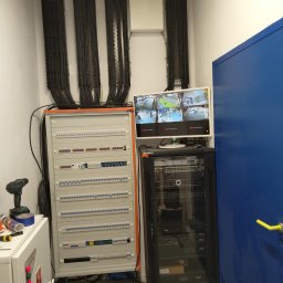 SMART EKO KAMIL WALASZKIEWICZ - Rozdzielnia elektryczna z monitoringiem na monitorze, kable w korytkach, szafa rack i narzędzia. Widok na instalacje w pomieszczeniu technicznym.