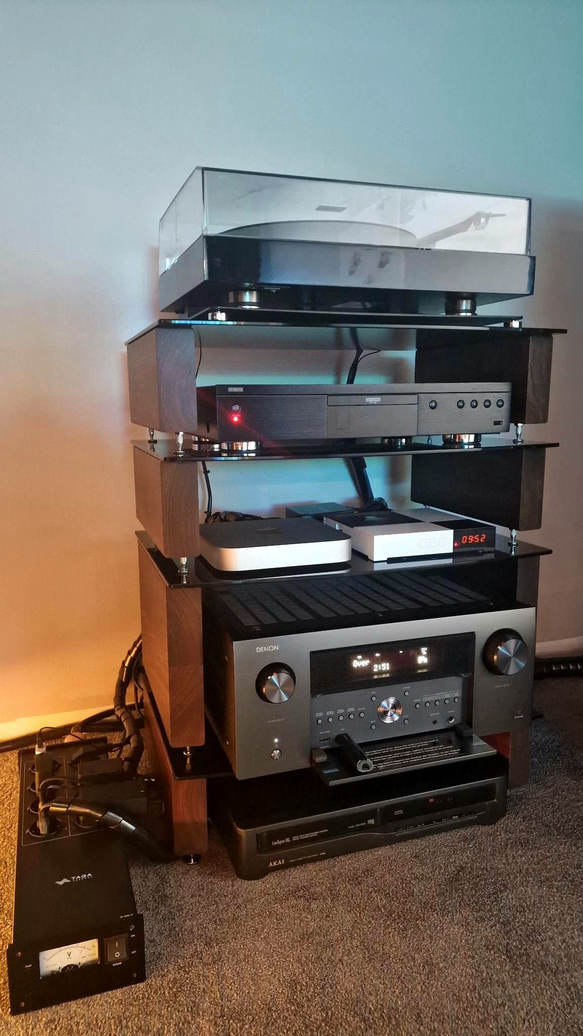 Wieża audio z gramofonem, odtwarzaczem CD i wzmacniaczem Denon na szklanych półkach z drewnianymi wspornikami. Widoczne kable i sprzęt audio na podłodze.