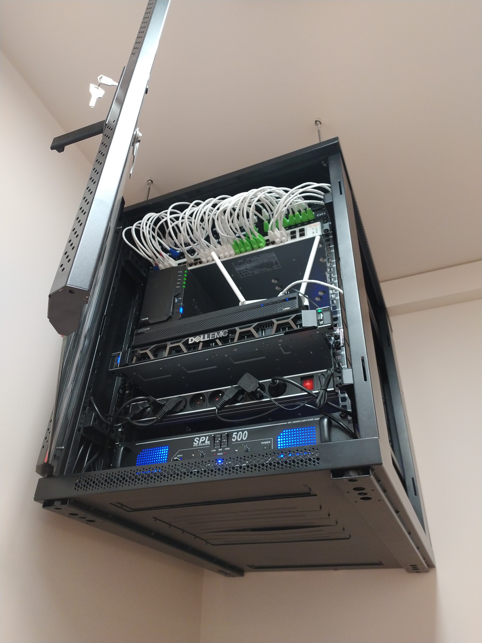 Zamontowana szafa rack z urządzeniami sieciowymi (router, switch) i kablami. Widok z dołu, szafa przymocowana do sufitu, kable uporządkowane.