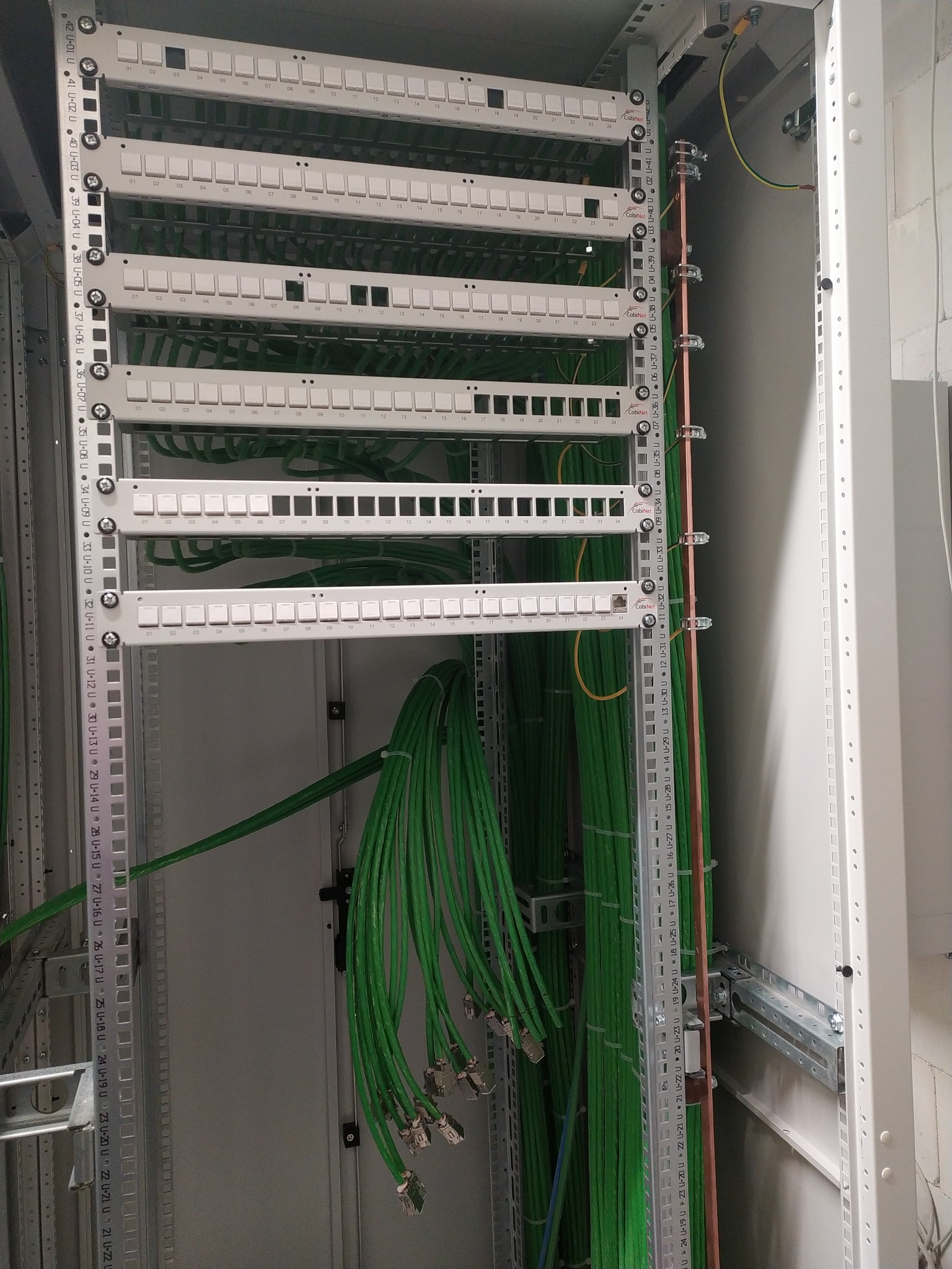 Panel krosowniczy z zielonymi kablami sieciowymi, widoczne oznaczenia portów i listwy montażowe w szafie rack. Instalacja teleinformatyczna w serwerowni.