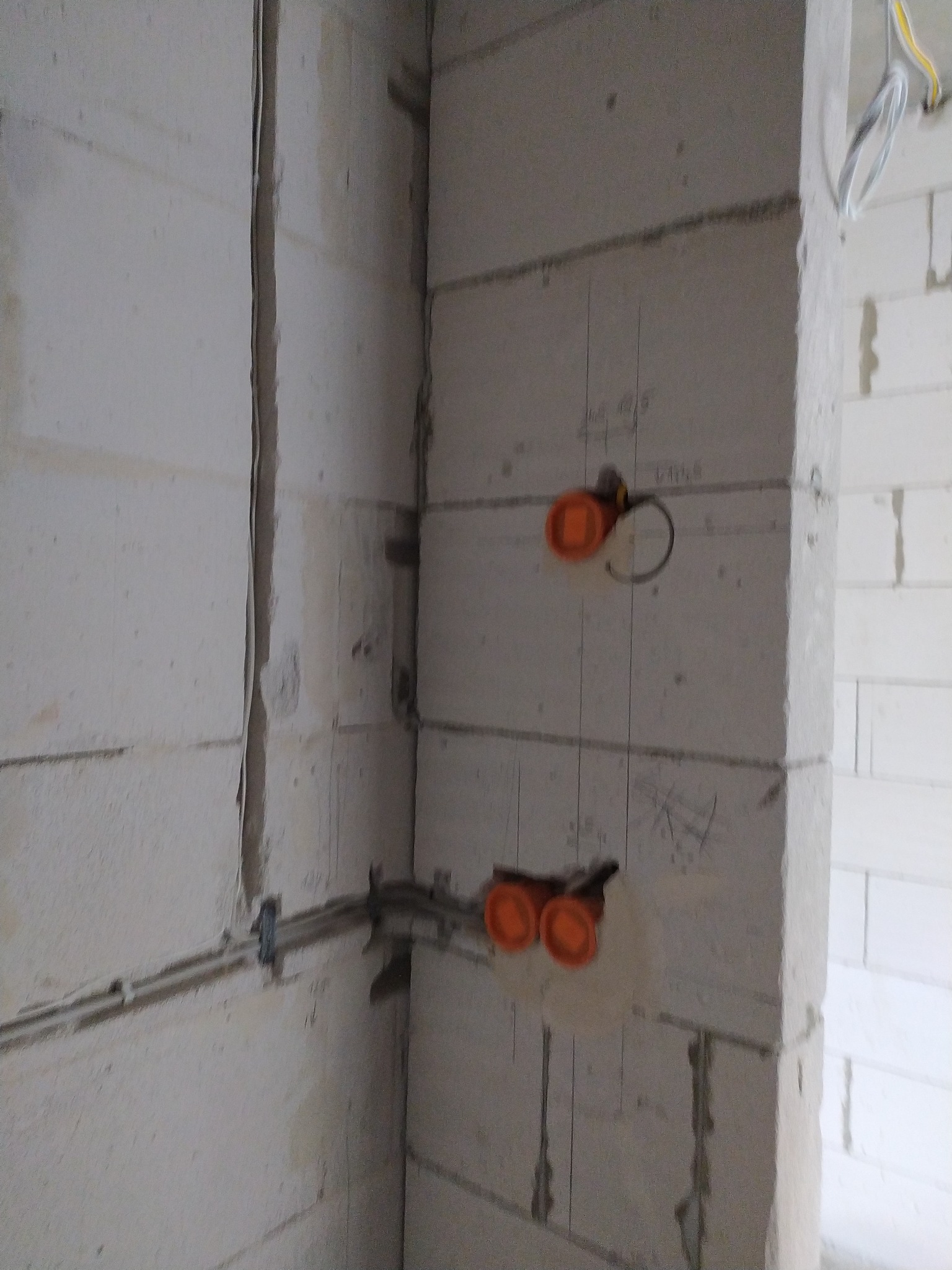 Surowa ściana z betonu komórkowego z zamontowanymi puszkami elektrycznymi w kolorze pomarańczowym i poprowadzonymi przewodami. Widoczne pionowe linie pomocnicze.