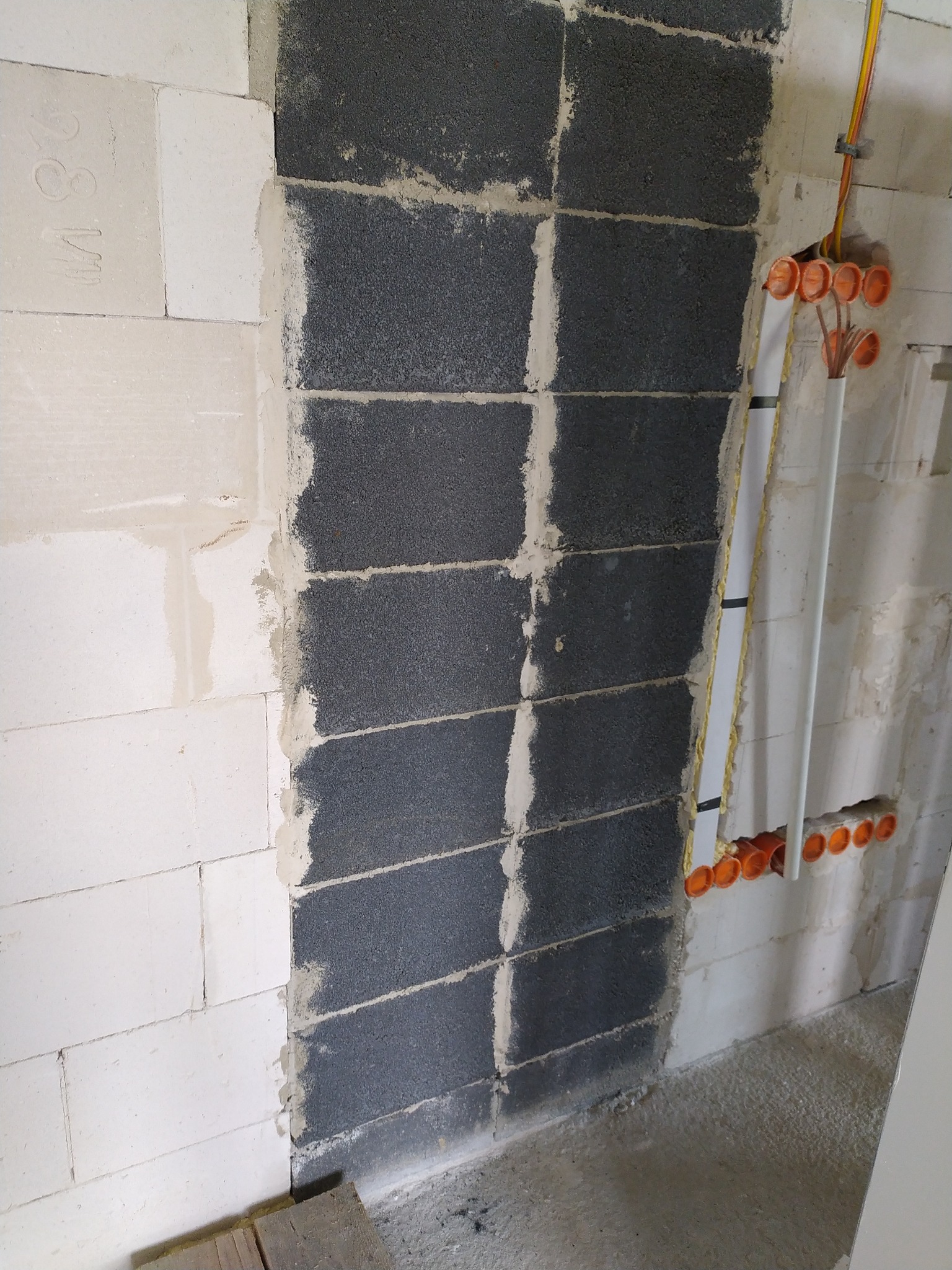 Ściana z pustaków z widocznymi puszkami instalacyjnymi i przewodami. Etap prac instalacyjnych w nowym budynku. Widoczne materiały budowlane i elementy instalacji.