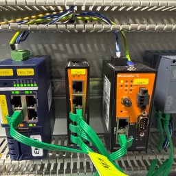 Rostyslav Loichenko - Panel sterowniczy z zamontowanymi modułami sieciowymi Weidmüller i Ewon, połączonymi zielonymi kablami Ethernet. Widoczne oznaczenia i diody LED.