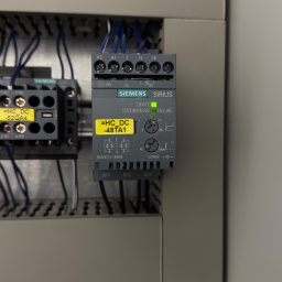 Rostyslav Loichenko - Szara szafa sterownicza z zamontowanym modułem Siemens Sirius z podłączonymi przewodami. Widoczna żółta naklejka z oznaczeniem modułu. Zielona dioda sygnalizuje stan pracy.