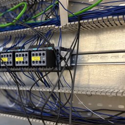 Rostyslav Loichenko - Szczegółowe ujęcie szafy sterowniczej z zamontowanymi stycznikami Siemens Sirius, okablowaniem w kolorach niebieskim i zielonym oraz szyną montażową.