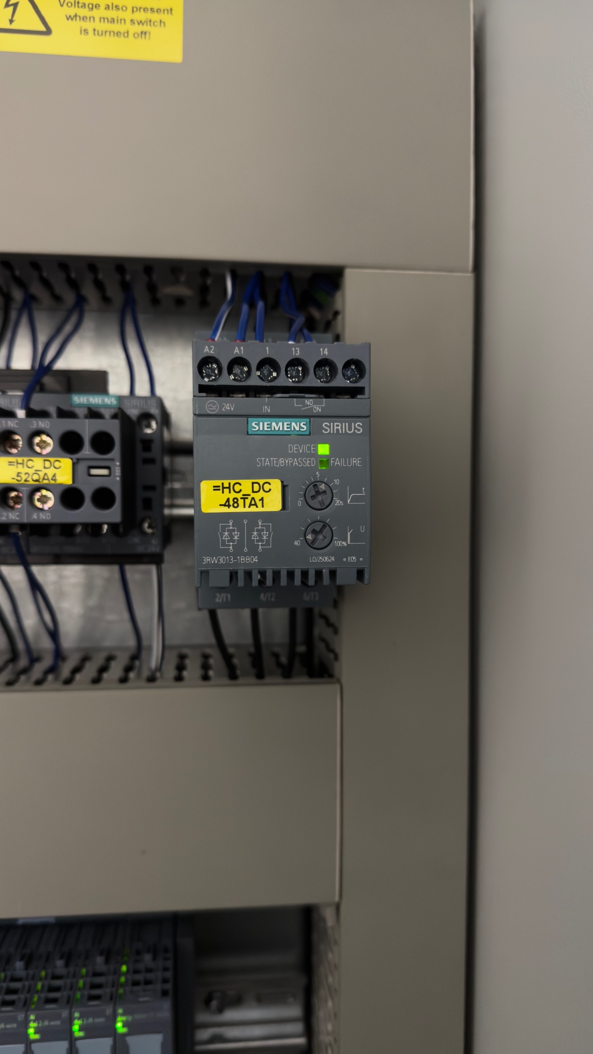 Szara szafa sterownicza z zamontowanym modułem Siemens Sirius z podłączonymi przewodami. Widoczna żółta naklejka z oznaczeniem modułu. Zielona dioda sygnalizuje stan pracy.