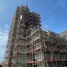 Rusztowania - Construct Services - Kościół w rusztowaniach pod błękitnym niebem. Widoczne drabiny i elementy konstrukcyjne rusztowań. Prace renowacyjne na wysokościach.