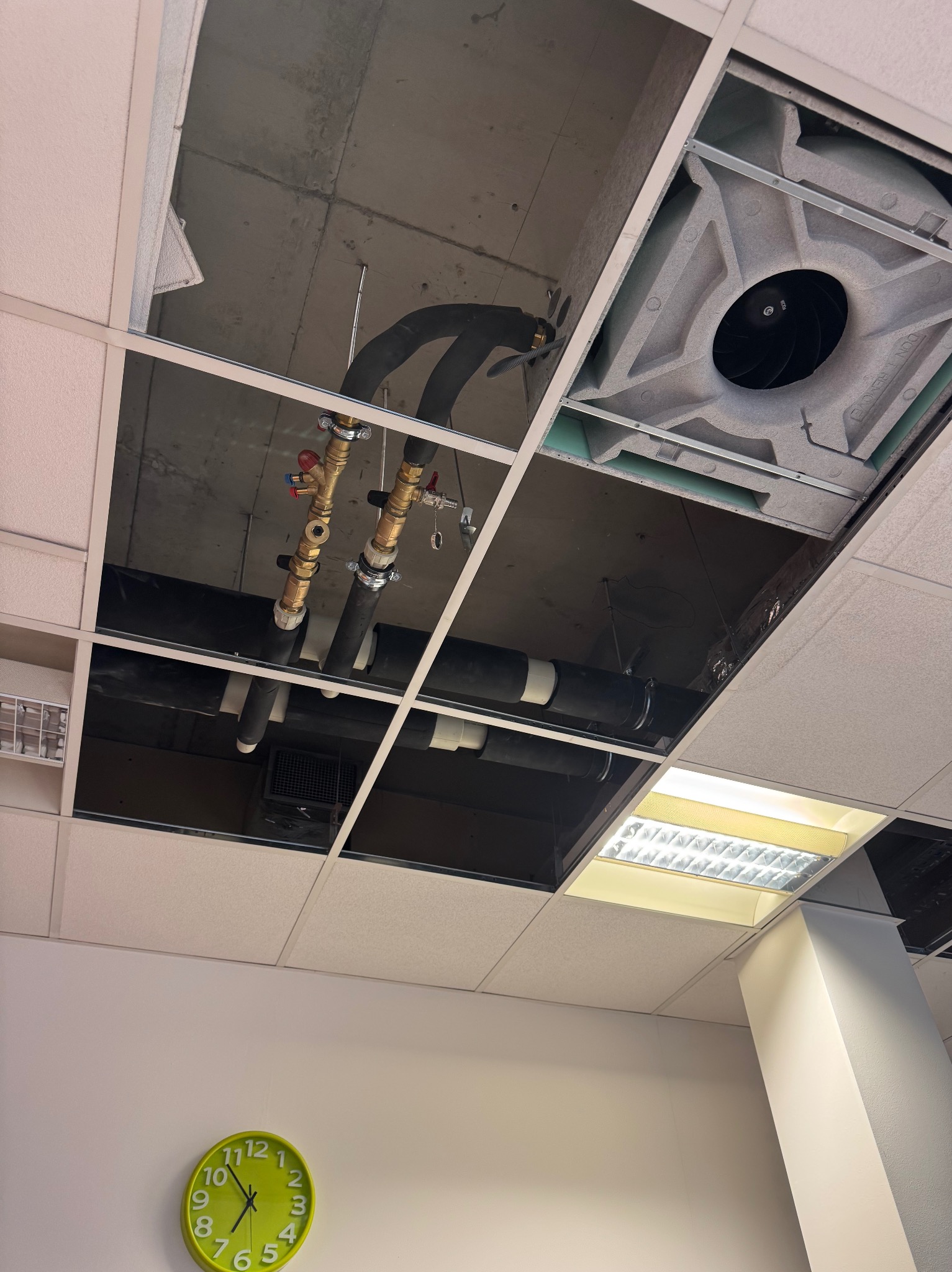 Odsłonięty sufit podwieszany z widocznymi rurami instalacji hydraulicznej, wentylacją i oświetleniem. Widoczny zegar na ścianie.