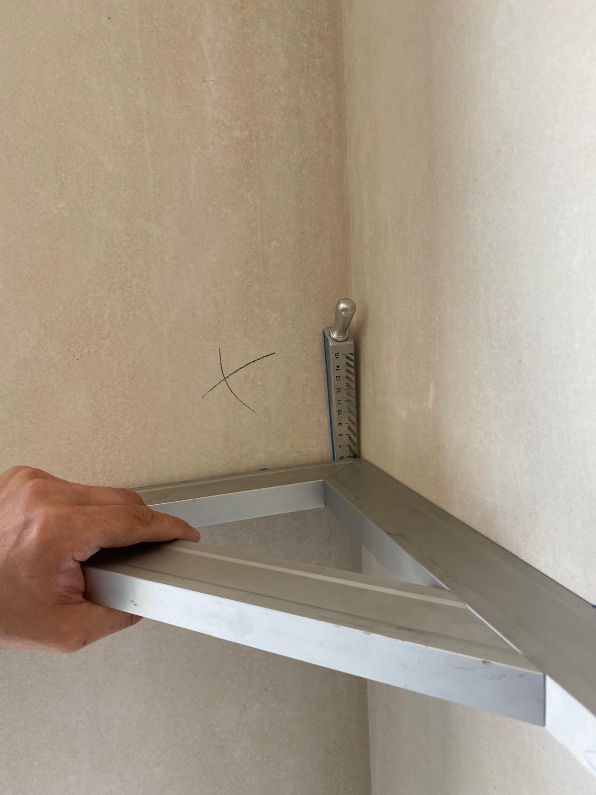 Pomiar kąta w rogu pomieszczenia za pomocą kątownika aluminiowego i poziomicy. Na ścianie widoczny znak ołówkiem.