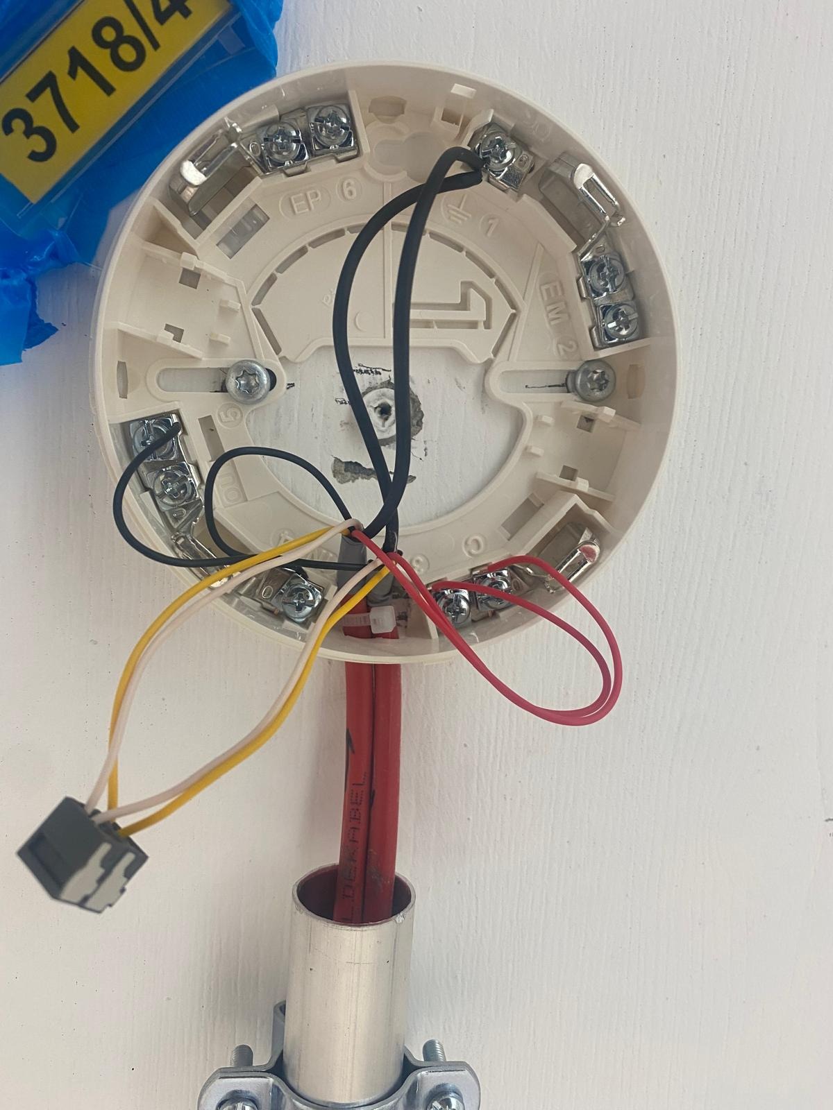 Podłączenie przewodów do białej podstawy czujnika, widoczne kolorowe kable (czerwony, żółty, czarny) i metalowe zaciski. Instalacja elektryczna w trakcie montażu.