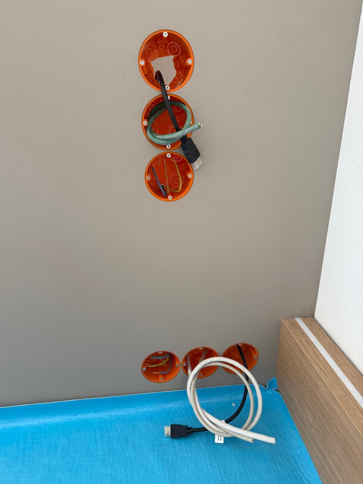 Montaż puszek elektrycznych w suficie podwieszanym z wystającymi przewodami i kablem HDMI. Widoczne zabezpieczenie folią. Prace instalacyjne w trakcie.