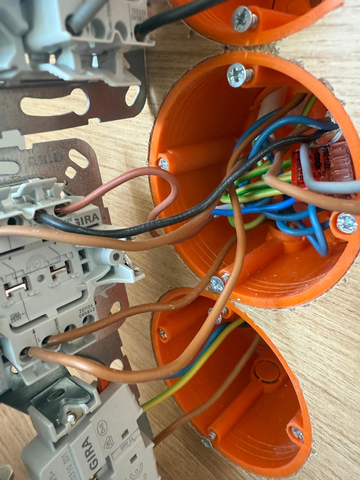 Pomarańczowe puszki elektryczne w ścianie z widocznymi przewodami i elementami montażowymi GIRA. Instalacja elektryczna w trakcie realizacji.