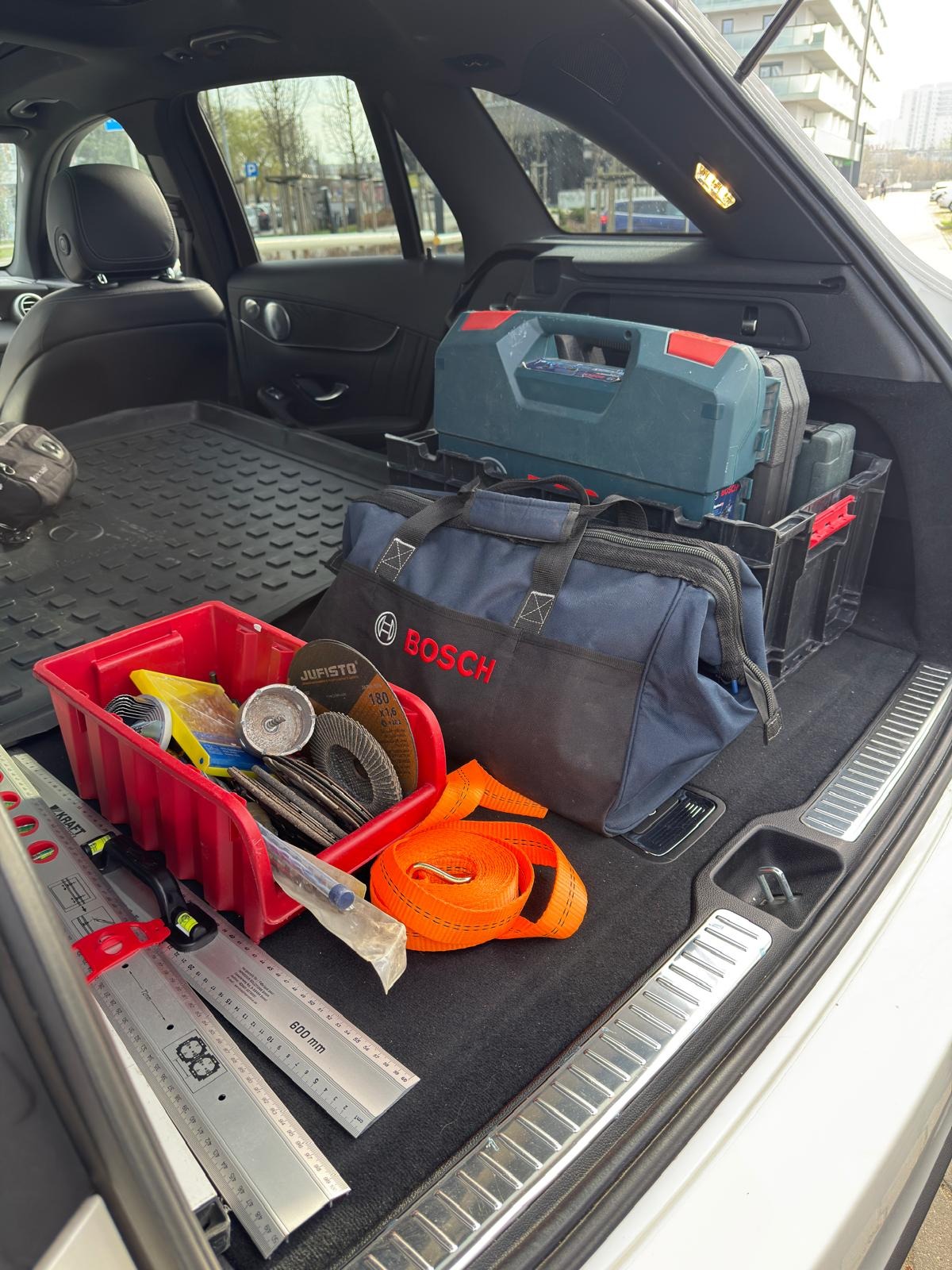 Otwarty bagażnik samochodu wypełniony narzędziami: skrzynka, torba Bosch, poziomice, tarcze do cięcia i pasy transportowe. Gotowość do pracy.